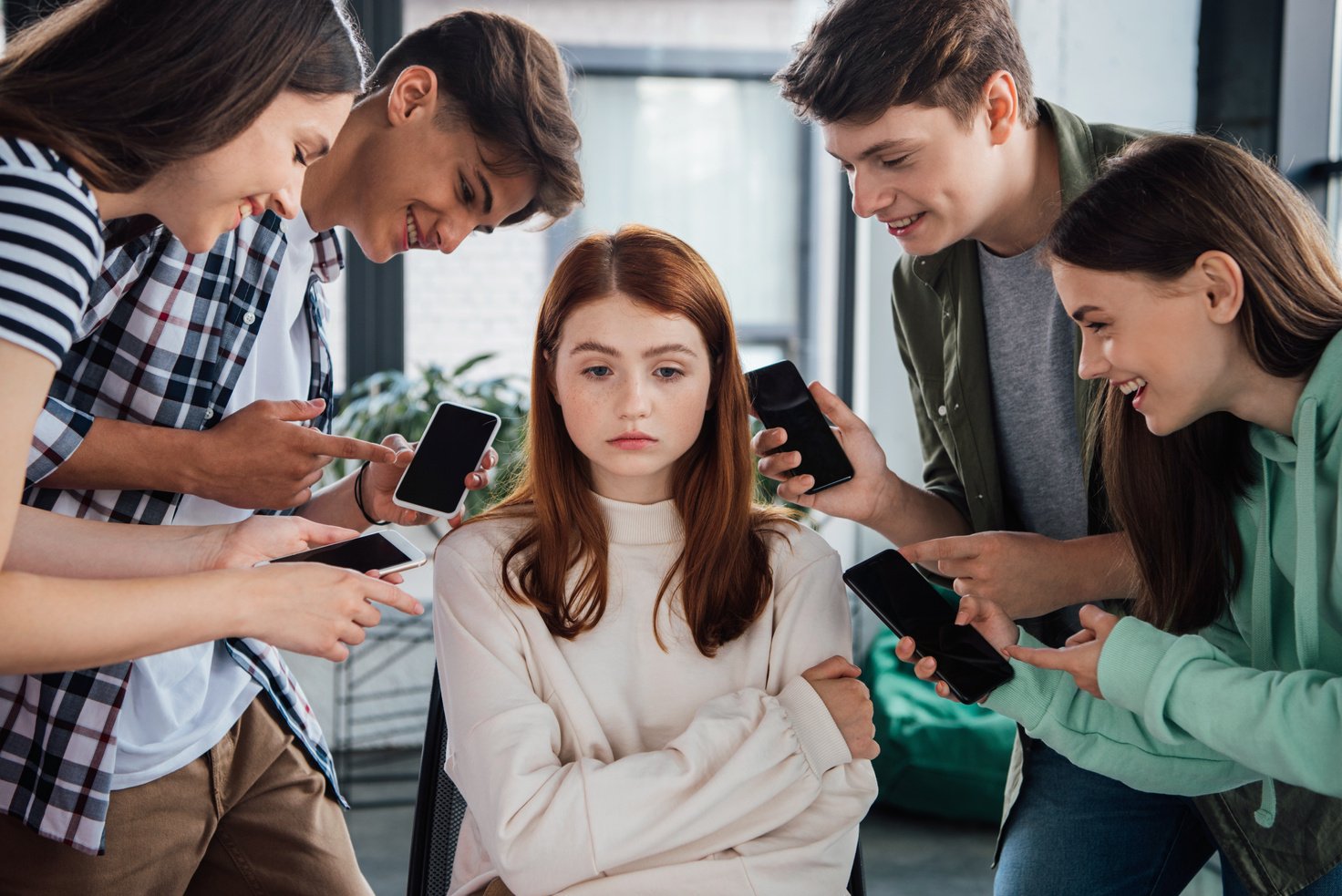 smiling teenagers pointing with fingers at girl during bullying and holding smartphones with blank screen